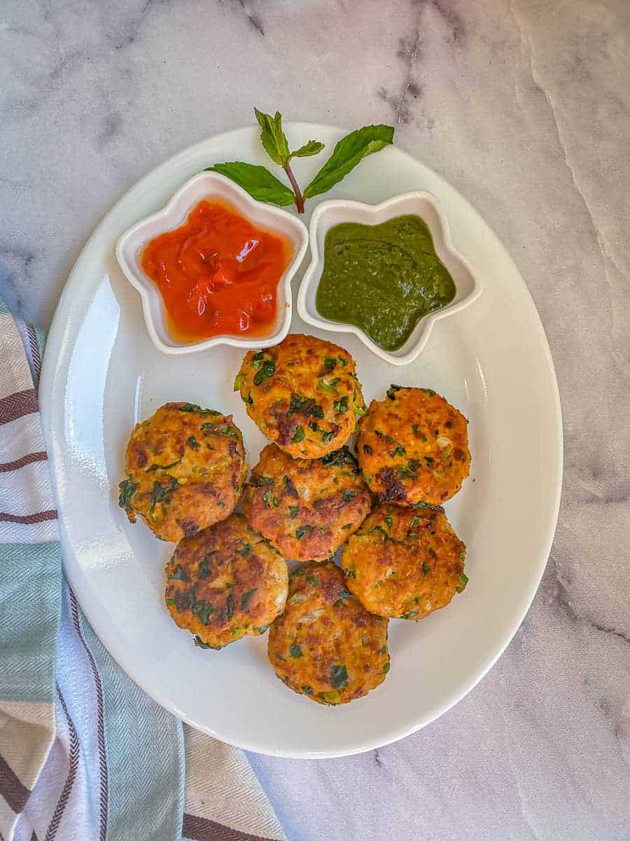 A plate of ground chicken cutlets, and bowls of coriander chutney and ketchup.