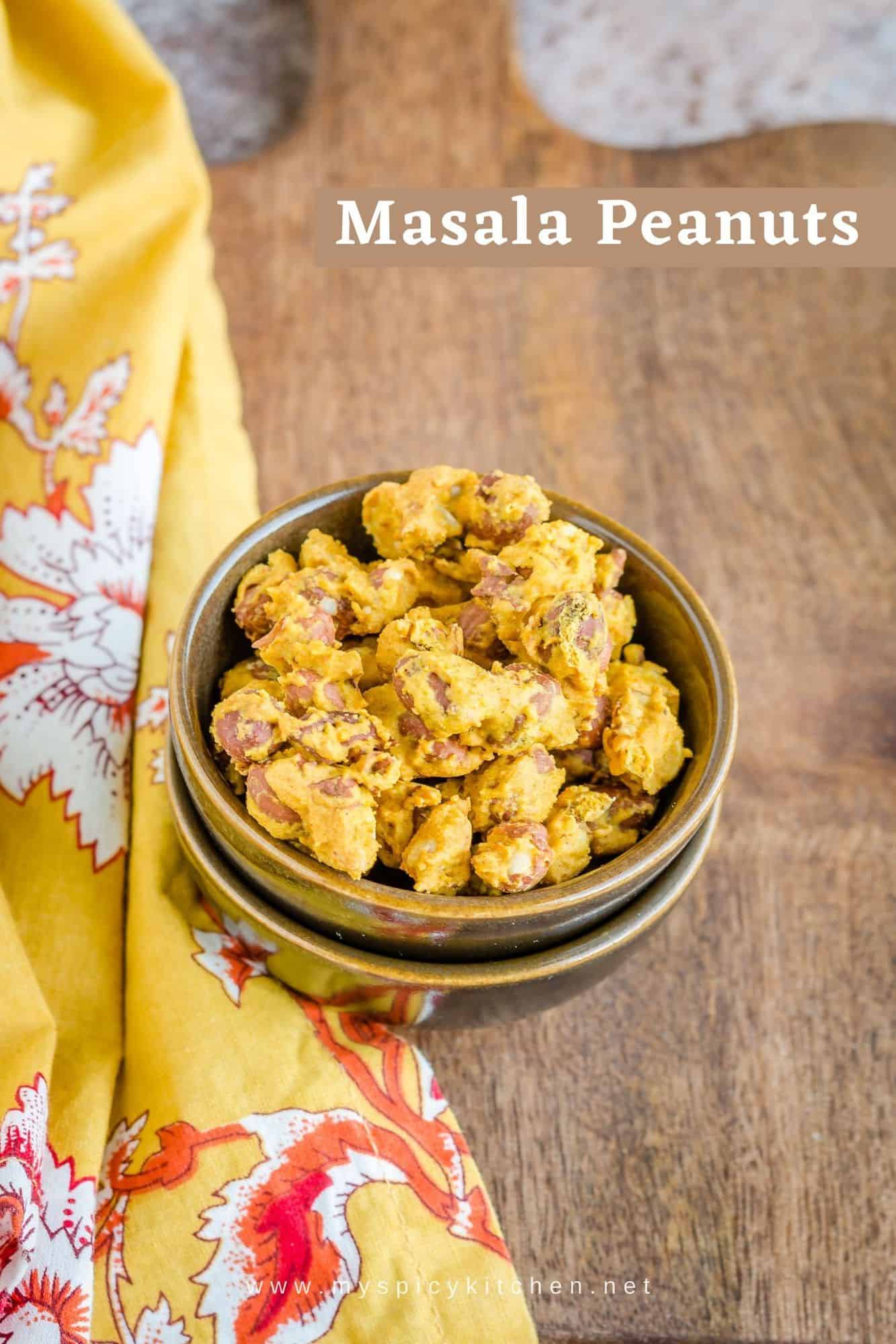Baked masala peanuts in a bowl, on a wooden board and a napkin on the left side of the bowl.