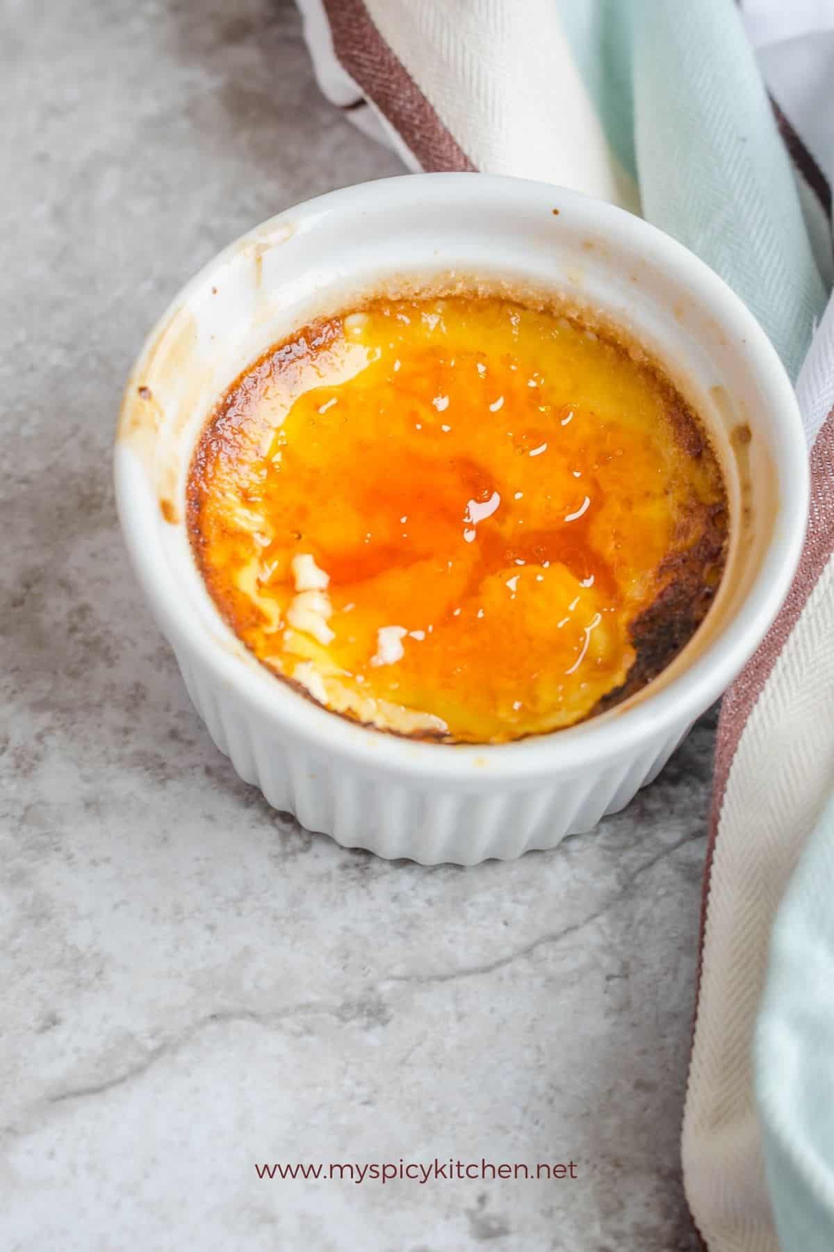 Ramekin of French caramel custard and a part of kitchen towel on the right.