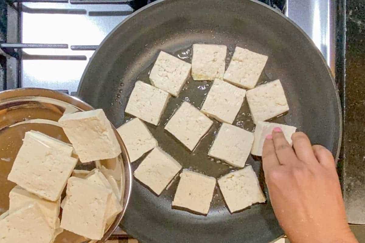 Placing sliced tofu in a frying pan.